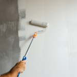 A person applying primer to a wall using a roller.